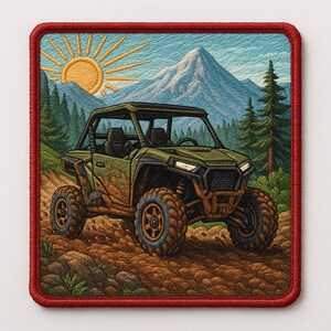 May include: Embroidered patch featuring an off-road vehicle driving through a mountain landscape. The patch has a red border and depicts a green ATV with mud splatters, a bright sun, and a snow-capped mountain in the background. The design evokes adventure and outdoor activities.