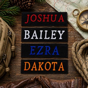 May include: Four rectangular black fabric patches with embroidered names. The top patch features the name JOSHUA in red, the second BAILEY in white, the third EZRA in blue, and the bottom patch displays the name DAKOTA in orange lettering.