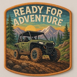 Puede incluir: Parche bordado con el texto "READY FOR ADVENTURE" sobre un vehículo todoterreno en un camino de tierra. El fondo presenta una cordillera, árboles y un sol poniente. El parche tiene un borde marrón.