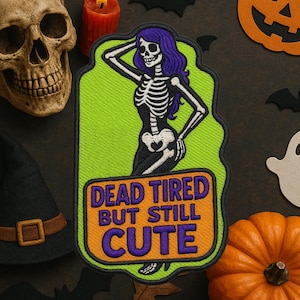 May include: Embroidered patch featuring a skeleton with purple hair, posed in a confident stance, set against a lime green background. The patch includes the text "DEAD TIRED BUT STILL CUTE" in purple and orange. Halloween-themed.