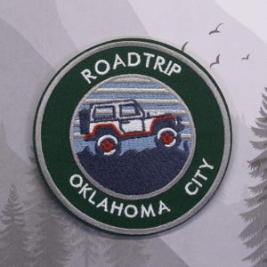May include: A green and white embroidered patch with a white jeep driving on a blue and white striped background. The text "ROADTRIP OKLAHOMA CITY" is around the jeep.