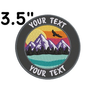 May include: A 3.5 inch embroidered patch with a mountain scene. The patch features a sunset with a flying bird, mountains, trees, and a lake. The text "YOUR TEXT" appears twice on the patch.