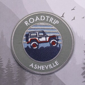 May include: A gray embroidered patch with a white jeep silhouette, blue and white stripes, and the text "ROADTRIP ASHEVILLE".