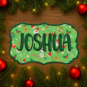 May include: A green embroidered patch with the name "JOSHUA" in dark green script. The patch has a decorative border and a festive pattern of Christmas icons. The background includes Christmas ornaments and pine branches.