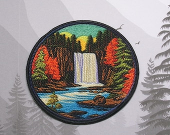 May include: Embroidered patch depicting a colourful scene of a waterfall flowing through a forest. The patch is circular and has a black border.