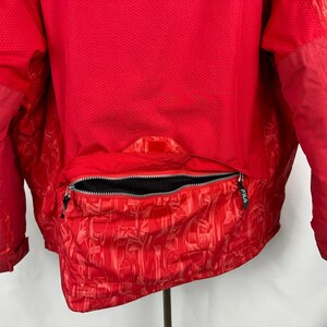 Puede incluir: Chaqueta roja brillante con un dise&ntilde;o texturizado. La chaqueta presenta una cremallera completa y una secci&oacute;n inferior estampada. La parte trasera de la chaqueta es visible, mostrando el dise&ntilde;o y la construcci&oacute;n. Prenda de abrigo deportiva.