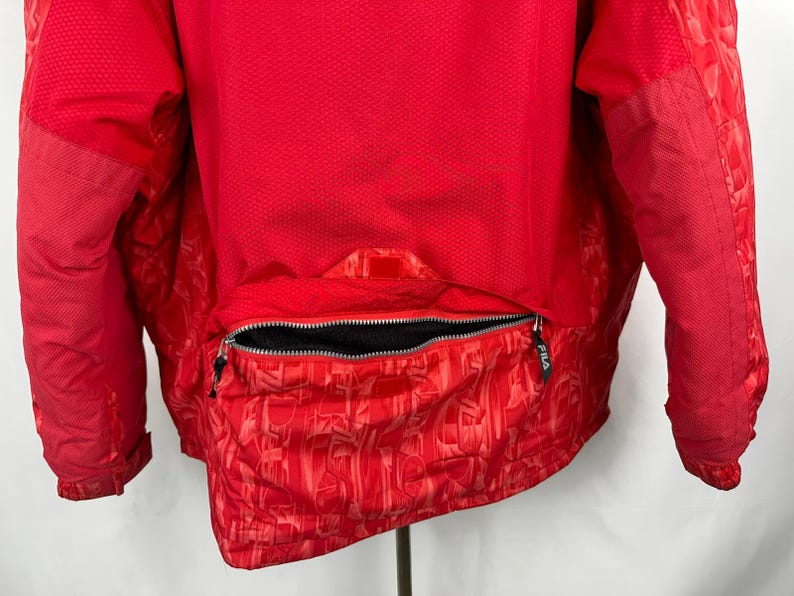 Puede incluir: Chaqueta roja brillante con un dise&ntilde;o texturizado. La chaqueta presenta una cremallera completa y una secci&oacute;n inferior estampada. La parte trasera de la chaqueta es visible, mostrando el dise&ntilde;o y la construcci&oacute;n. Prenda de abrigo deportiva.