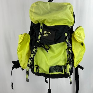 Può includere: Zaino nero e giallo neon con la scritta "PRO 150". Lo zaino ha più scomparti e cinghie regolabili. Ha due tasche laterali e una patta superiore. Lo zaino ha un'etichetta con "50" e "adidas".