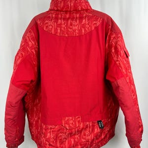 Puede incluir: Chaqueta de invierno roja brillante con cuello alto y forro interior azul. La chaqueta presenta un patr&oacute;n texturizado en los hombros y la parte inferior de la espalda, con un panel de malla en la parte superior de la espalda. El logotipo de Fila es visible en la parte inferior derecha.