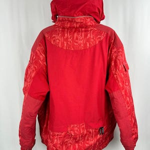 Puede incluir: Una chaqueta de invierno roja brillante con capucha. La chaqueta presenta una mezcla de texturas, incluyendo un patr&oacute;n acolchado en las mangas y un material similar a una malla en la espalda. Tiene cierre de cremallera y un peque&ntilde;o bolsillo en la manga.