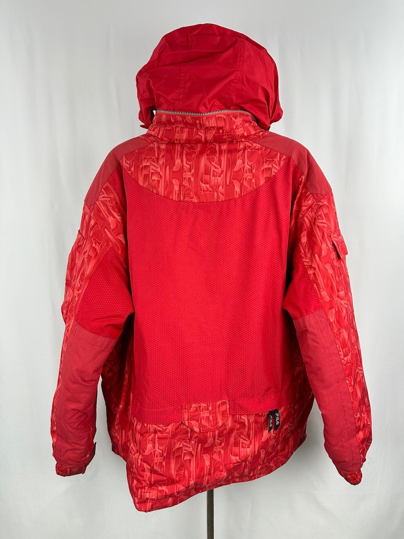 Puede incluir: Una chaqueta de invierno roja brillante con capucha. La chaqueta presenta una mezcla de texturas, incluyendo un patr&oacute;n acolchado en las mangas y un material similar a una malla en la espalda. Tiene cierre de cremallera y un peque&ntilde;o bolsillo en la manga.