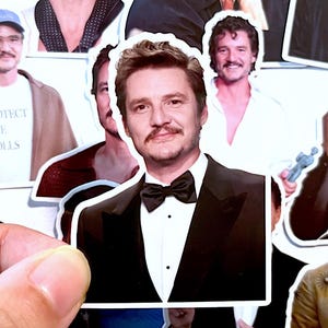 May include: A collection of stickers featuring a man in various poses. One sticker shows the man in a black tuxedo with a bow tie. Other stickers show the man in a white t-shirt with the text "PROTECT THE DOLLS".