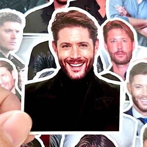 May include: A collection of stickers featuring a smiling man with brown hair and a beard. The stickers vary in size and show the man in different poses and outfits. The background is a mix of other stickers and a hand holding one.