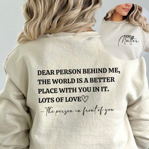 May include: A beige sweatshirt with the text "DEAR PERSON BEHIND ME, THE WORLD IS A BETTER PLACE WITH YOU IN IT. LOTS OF LOVE♡ - The person in front of you" printed on the back.