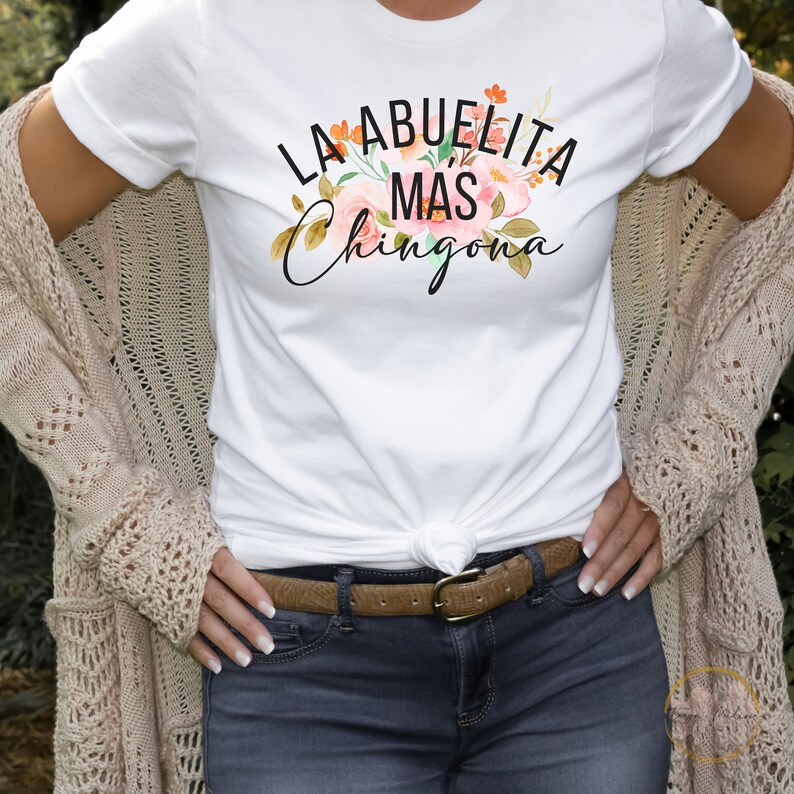 May include: White t-shirt with the text "La Abuelita Mas Chingona" in black lettering with a floral design.