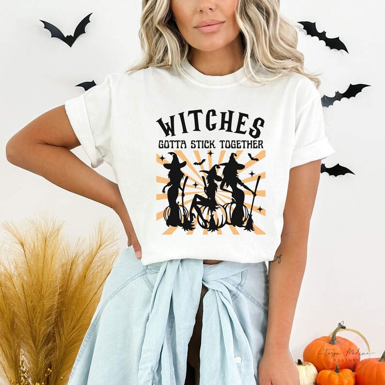 Puede incluir: Camiseta blanca con un gr&aacute;fico negro de tres brujas en escobas con el texto "Witches Gotta Stick Together".