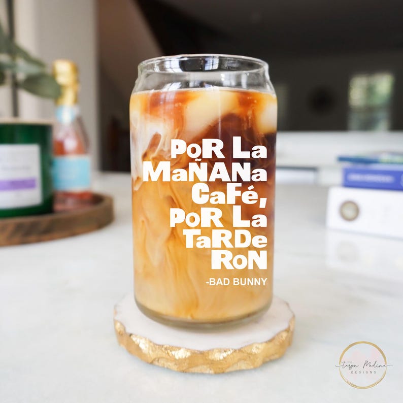 May include: A glass of iced coffee in a can-shaped glass with the text "Por La Ma&ntilde;ana Caf&eacute;, Por La Tarde Ron -Bad Bunny" printed on the side.