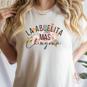 May include: A white t-shirt with a floral design and the text "La Abuelita Mas Chingona" in black.