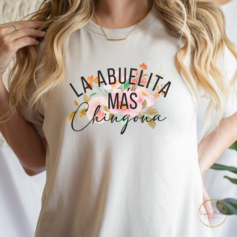 May include: A white t-shirt with a floral design and the text "La Abuelita Mas Chingona" in black.