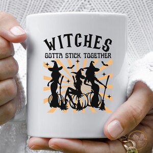Puede incluir: Taza de cer&aacute;mica blanca con una silueta negra de tres brujas montando escobas con el texto "Witches Gotta Stick Together".