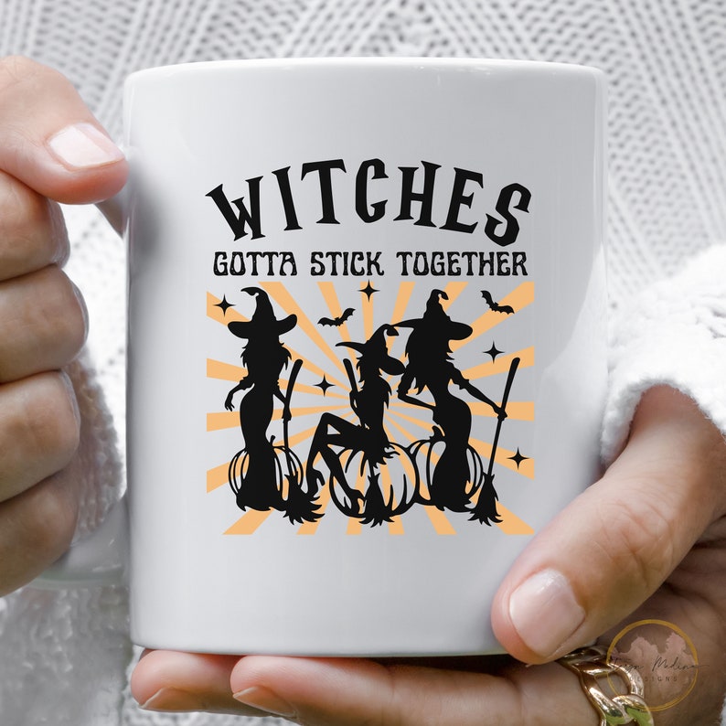 Puede incluir: Taza de cer&aacute;mica blanca con una silueta negra de tres brujas montando escobas con el texto "Witches Gotta Stick Together".