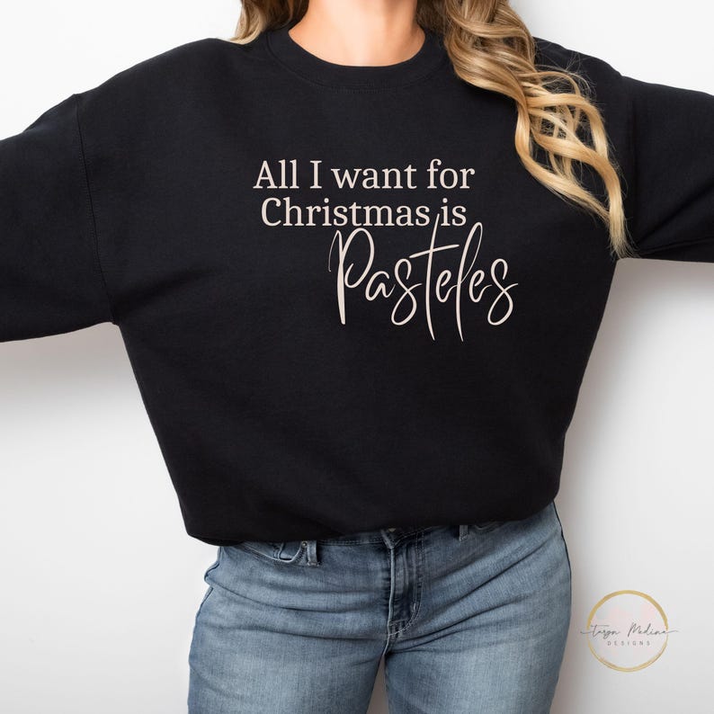May include: Black sweatshirt with the text "All I want for Christmas is Pasteles" in white lettering.