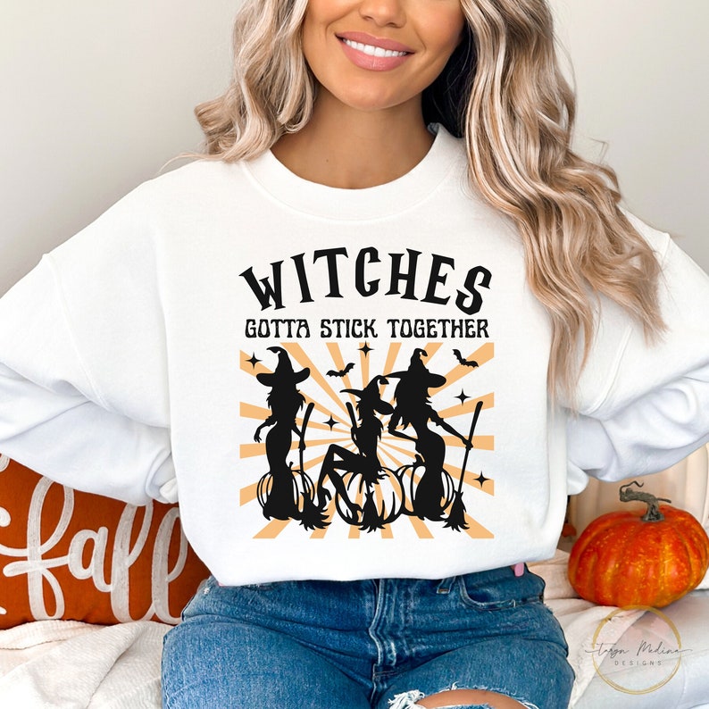 Puede incluir: Sudadera blanca con un gr&aacute;fico negro de tres brujas con escobas y calabazas. El texto "Witches Gotta Stick Together" est&aacute; impreso en negro sobre el gr&aacute;fico.