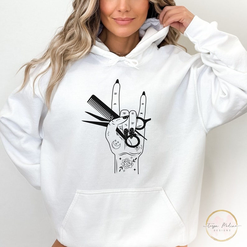 Peut inclure: Sweat-shirt blanc avec un motif noir d'une main tenant des ciseaux et un peigne dans un geste de rock and roll. La main est tatou&eacute;e avec une lune croissante, des &eacute;toiles et une rose.