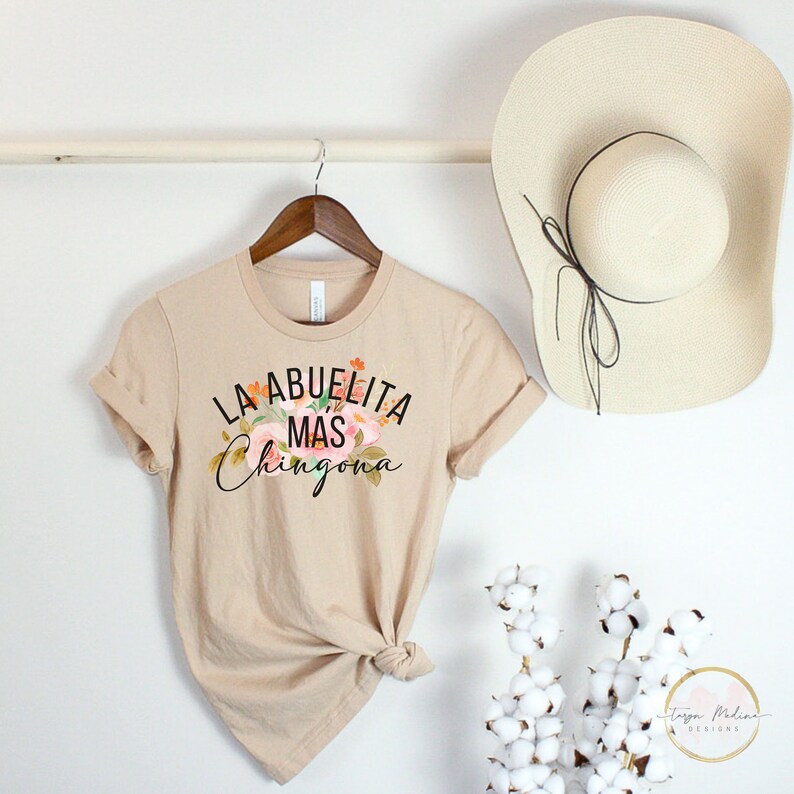 May include: A beige t-shirt with a floral design and the text "La Abuelita Mas Chingona" in black.