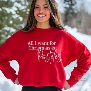 May include: Red sweatshirt with white text that reads "All I want for Christmas is Pasteles".