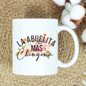 May include: White ceramic mug with a floral design and the text "LA ABUELITA MAS CHINGONA" in black.
