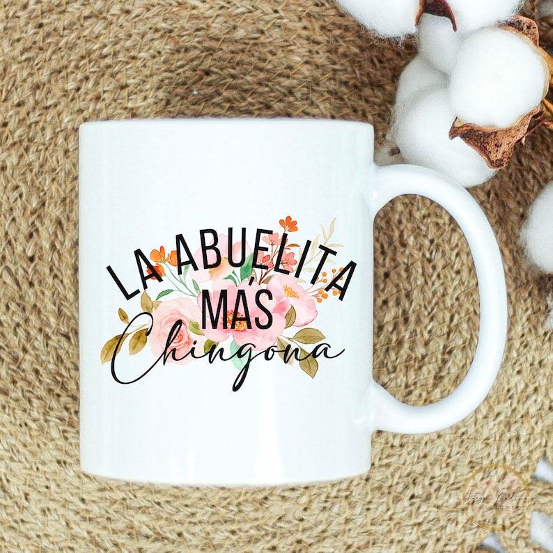 May include: White ceramic mug with a floral design and the text "LA ABUELITA MAS CHINGONA" in black.