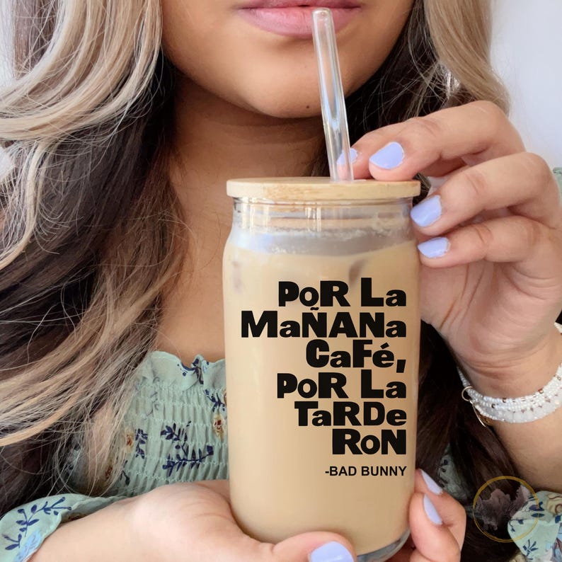 May include: A clear glass jar with a bamboo lid and a black and white graphic that reads "Por La Ma&ntilde;ana Caf&eacute;, Por La Tarde Ron -Bad Bunny". The jar is filled with a light brown liquid and a clear plastic straw is sticking out of the top.