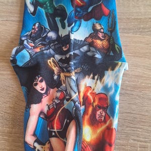 May include: A pair of blue socks featuring a colorful graphic of DC Comics superheroes, including Superman, Batman, Wonder Woman, and The Flash. The socks have black toes and heels, and the design covers the entire sock.