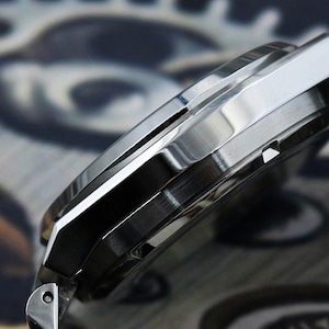 May include: Close-up of a silver wristwatch with a polished metal band. The watch case has a sleek, angular design with a brushed finish. The watch face is not visible in this side view.
