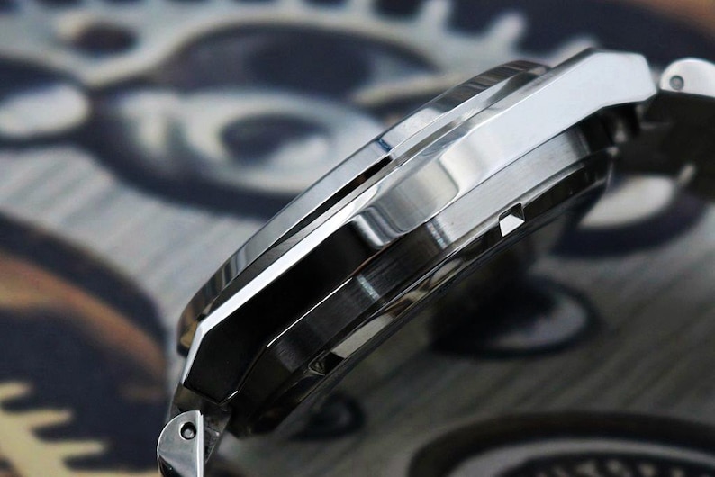 May include: Close-up of a silver wristwatch with a polished metal band. The watch case has a sleek, angular design with a brushed finish. The watch face is not visible in this side view.