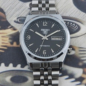 May include: A set of three ceramic mugs with a speckled, matte finish. The mugs are in shades of cream, light gray, and dark gray. Each mug has a simple, minimalist design and a rounded handle. Perfect for coffee or tea.