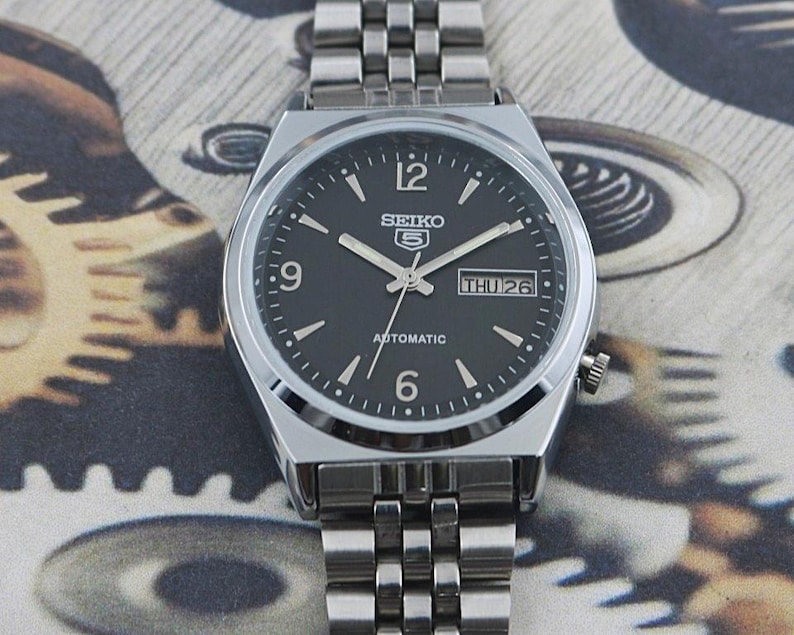 May include: A set of three ceramic mugs with a speckled, matte finish. The mugs are in shades of cream, light gray, and dark gray. Each mug has a simple, minimalist design and a rounded handle. Perfect for coffee or tea.