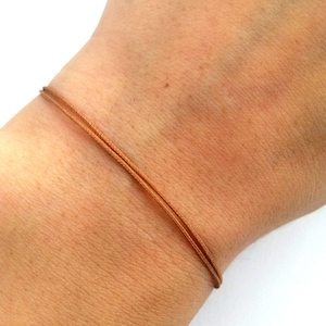 May include: A brown cord bracelet on a person's wrist.