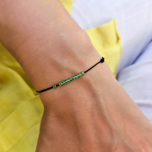 May include: A simple bracelet with a black cord and small green square beads.