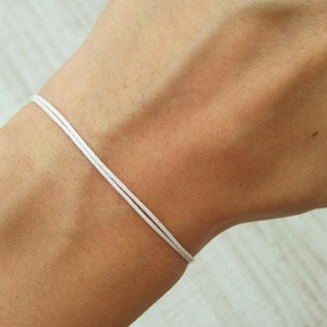 Puede incluir: Un brazalete de cuerda blanco usado en la muñeca.