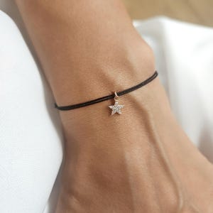May include: A black string bracelet with a small gold star charm set with clear cubic zirconia stones.