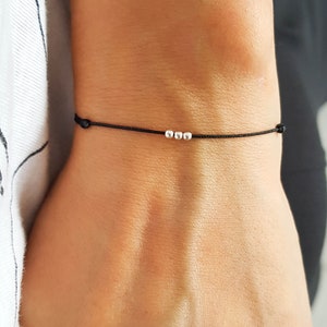Puede incluir: Un brazalete sencillo de cuerda negra con tres pequeñas cuentas plateadas.