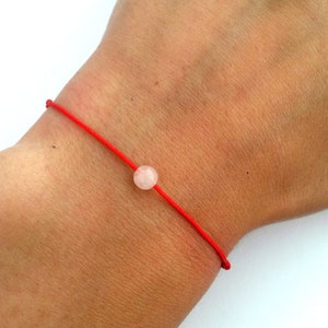 Könnte beinhalten: Ein rotes Armband mit einer einzigen, runden, hellrosa Edelsteinperle.