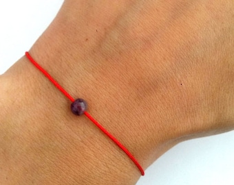 Pode incluir: Um bracelete de corda vermelha com um único contas de pedra preciosa de cor roxa escura.
