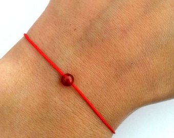 Könnte beinhalten: Ein rotes Armband mit einer kleinen, runden, dunkelroten Edelsteinperle.
