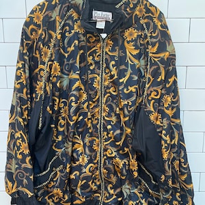 May include: Black and gold floral print jacket with a zipper closure and a Plus Factor label. The jacket has a gold chain trim around the edges.