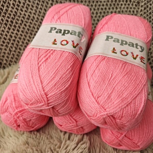 May include: Close-up of several pink yarn skeins, each labelled "Papaty LOVE". The yarn is a solid, bright pink. The skeins are arranged on a textured, neutral-toned surface, ideal for knitting or other crafts.