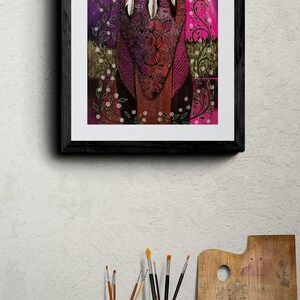 May include: Framed art print featuring a stylized illustration of three figures with feathers, set against a purple and pink night sky with a full moon. The artwork is framed in a black wooden frame.