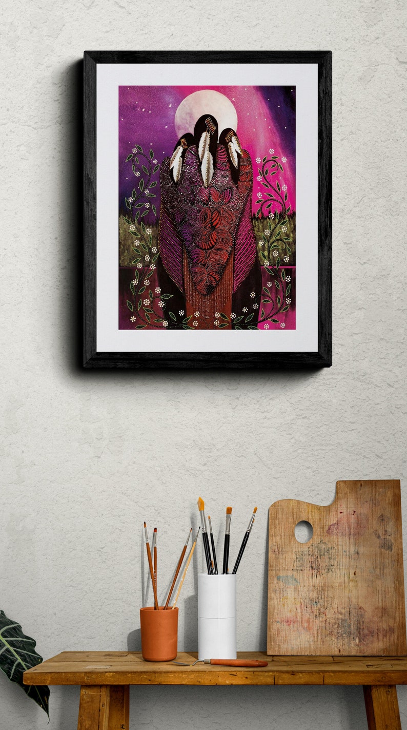 May include: Framed art print featuring a stylized illustration of three figures with feathers, set against a purple and pink night sky with a full moon. The artwork is framed in a black wooden frame.